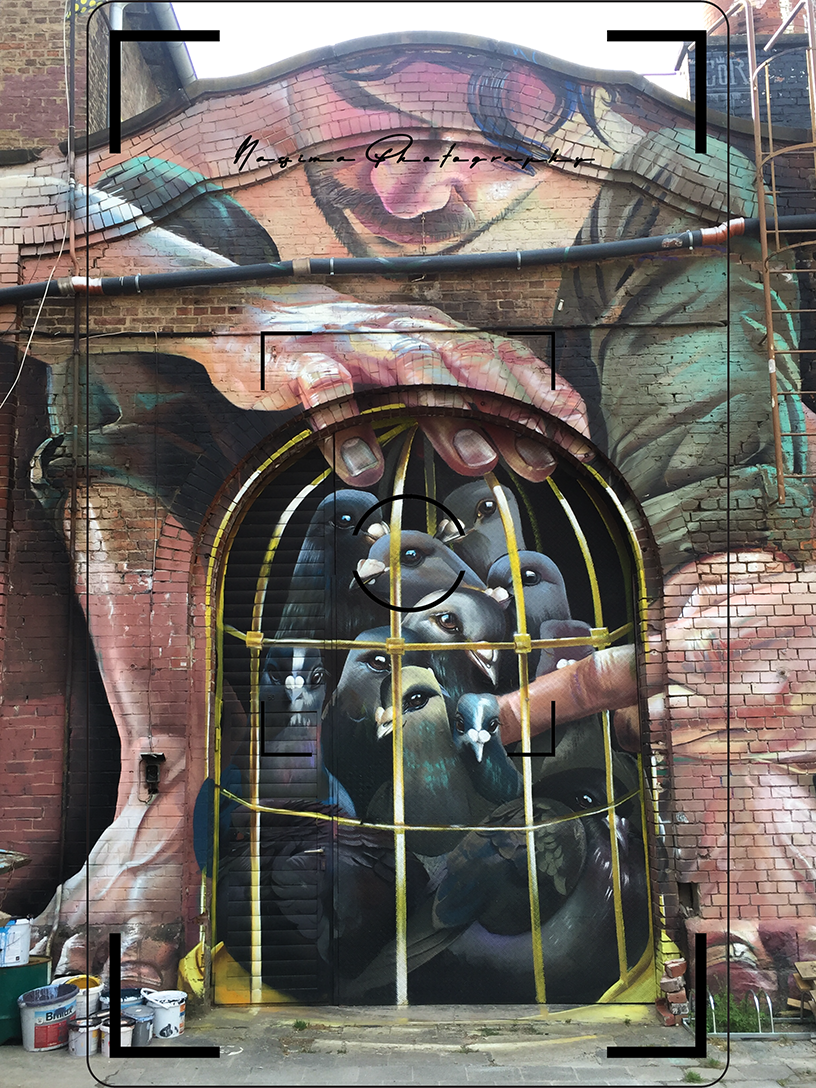 Großflächiges Graffiti mit eingesperrten Tauben an einer Backsteinfassade der Naxoshalle in Frankfurt am Main.